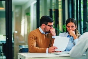 Portrait of a couple with financial problems looking at document in financial adviser's office.