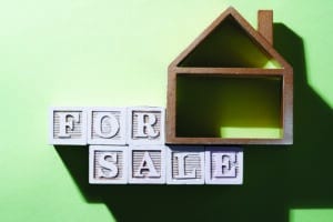 Model of a house with wooden letter blocks spelling out "for sale."