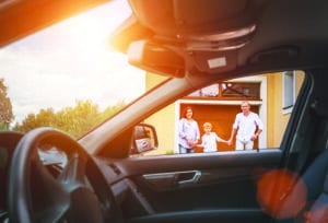 Young couple with little boy son goes to their car standing on the home yard inside car view