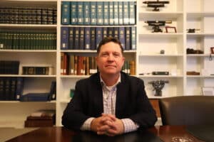 Executive Director of Construction Industries of Massachusetts Jeff Mahoney sits at a table in front of bookshelves staring confidently at the camera.